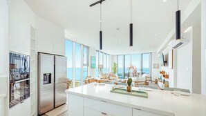 Une cuisine moderne dotée d’un grand îlot central, d’appareils électroménagers en acier inoxydable et offrant une vue sur l’océan.