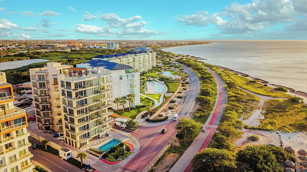 Un hotel de gran altura con varias plantas, una piscina y un paseo marítimo frente a la playa.