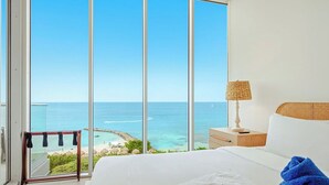 Une chambre avec une grande fenêtre donnant sur une plage et l’océan.