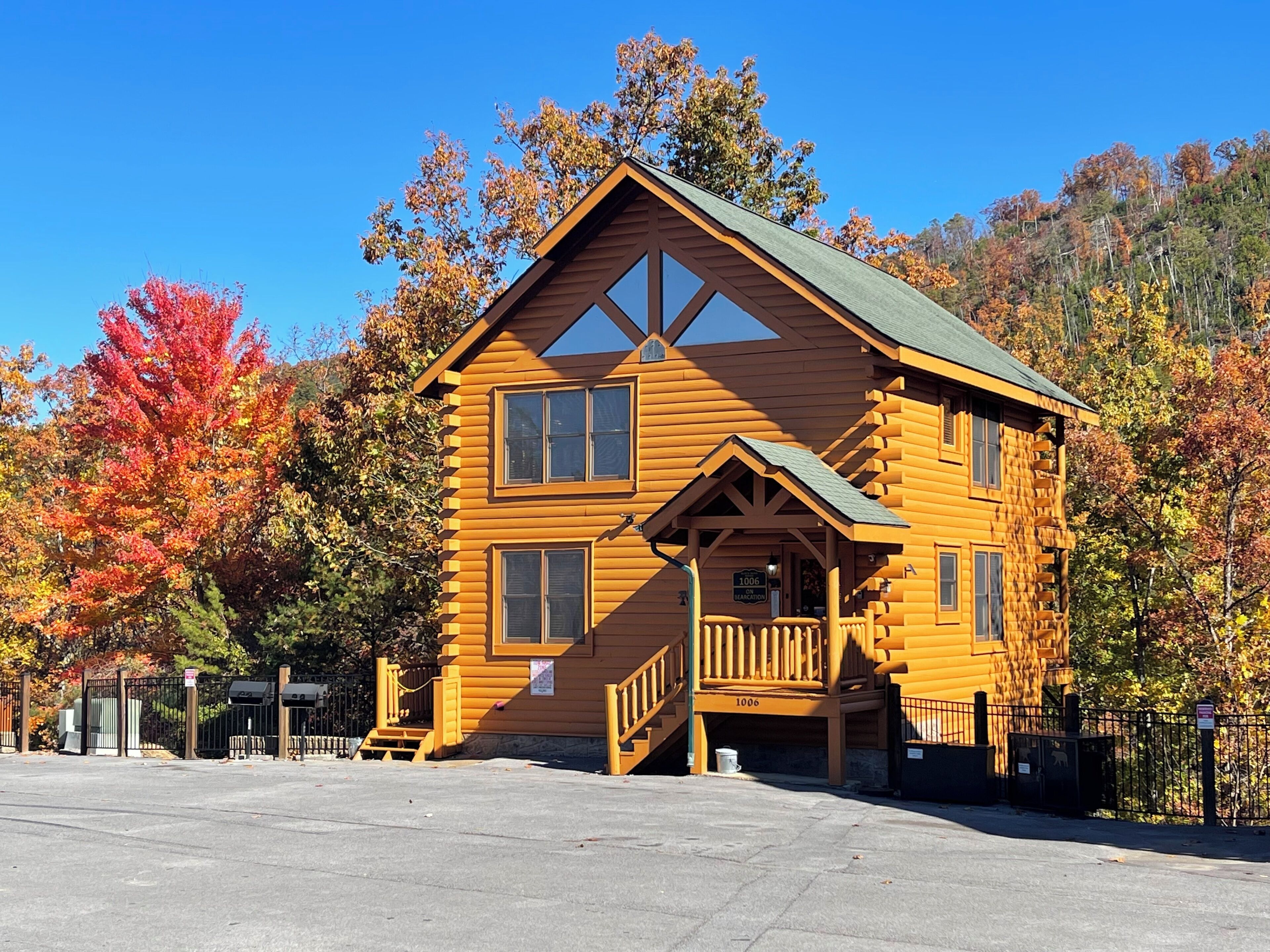 A wooden cabin with a porch and a small staircase, surrounded by autumn foliage.