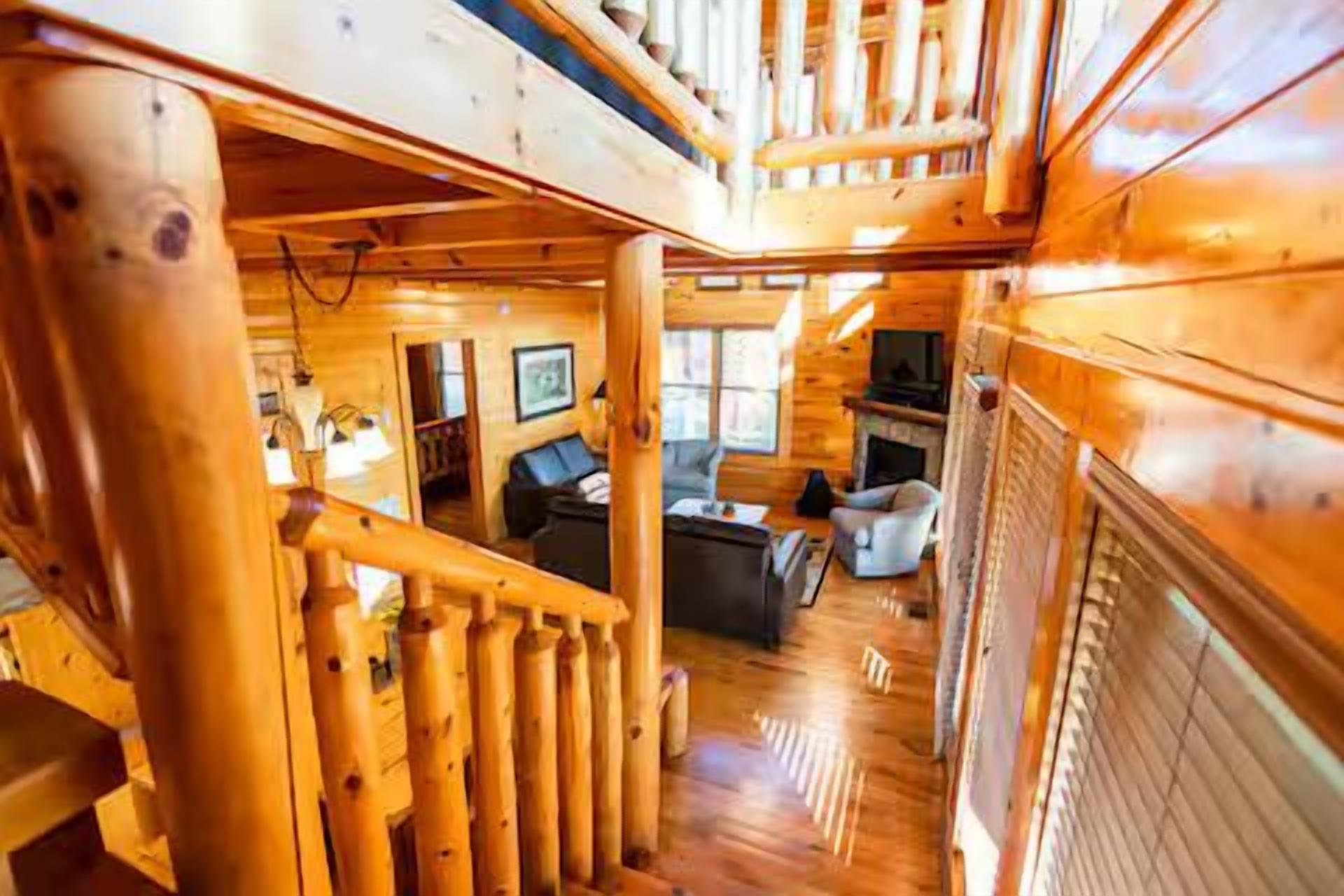 A wooden cabin interior with a staircase, a living room with a fireplace, and a dining area.