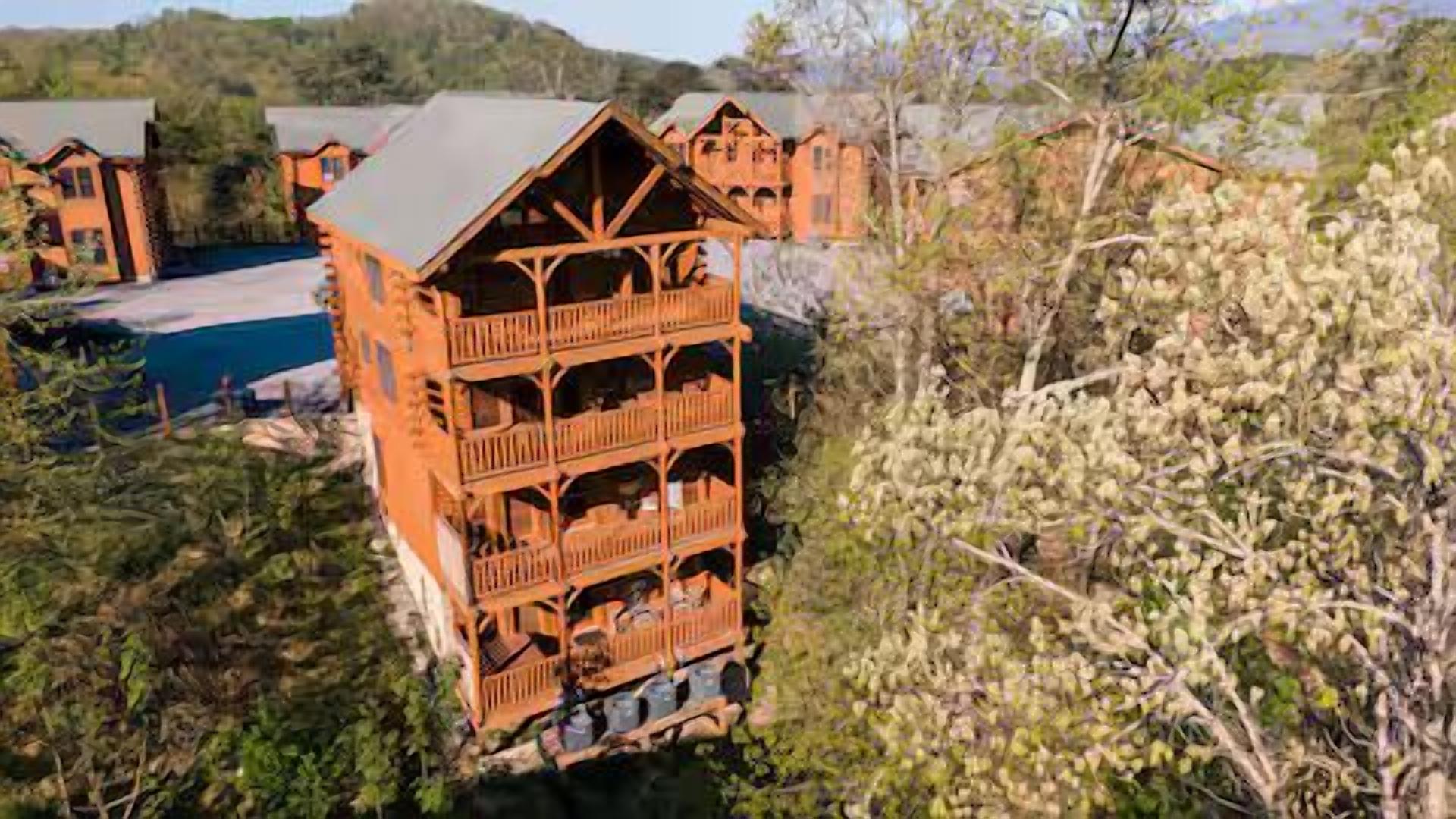 A multi-story wooden building with balconies, surrounded by greenery and a swimming pool.