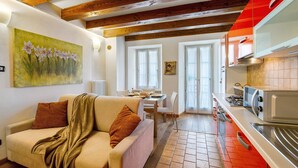 Una sala de estar con sofá, un cuadro, un comedor con mesa y sillas, y una cocina con electrodomésticos.