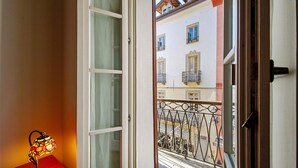 Un balcón con barandilla de hierro forjado, una ventana con cortina y una lámpara de mesa.