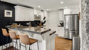 A modern kitchen with white cabinets, stainless steel appliances, and a central island with bar stools. - Modern Mountain Home Near Park City & Jordanelle (Kamas)