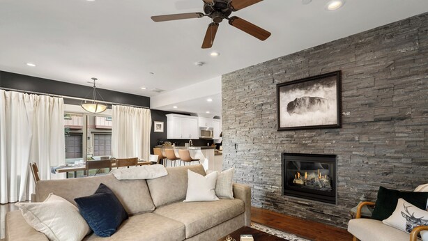 A modern living room with a stone fireplace, a ceiling fan, and a dining area in the background. - Modern Mountain Home Near Park City & Jordanelle (Kamas)