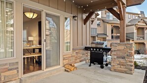 An outdoor patio with a grill, a dining area with a table and chairs, and a stone pillar. - Modern Mountain Home Near Park City & Jordanelle (Kamas)