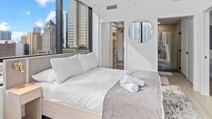 Un dormitorio moderno con un ventanal grande, un espejo redondo y un vestidor.