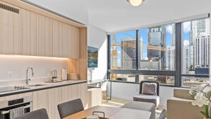 Una cocina moderna con armarios de madera, un comedor con mesa y sillas, y ventanas amplias con vista a la ciudad.