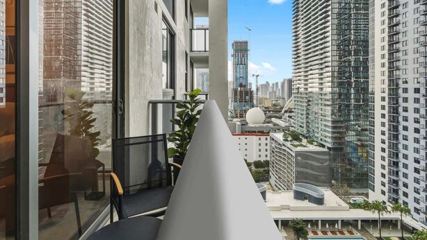 A modern hotel room with a balcony overlooking a cityscape, featuring a pool and lush greenery. - Downtown Miami Studio near Bayfront Park Pool (Miami)
