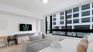 Een moderne hotelkamer met een groot raam, een flatscreen televisie, een bank en een bureau.