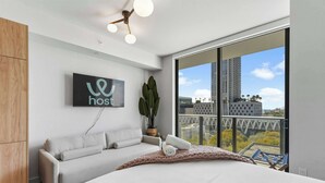 A modern hotel room with a large bed, a sofa, a plant, and a view of the cityscape. - Downtown Studio | Rooftop Pool & Skyline Views (Miami)