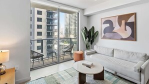 Ein modernes Wohnzimmer mit einem weißen Sofa, einem runden Couchtisch und einem großen Fenster mit Blick auf hohe Gebäude.