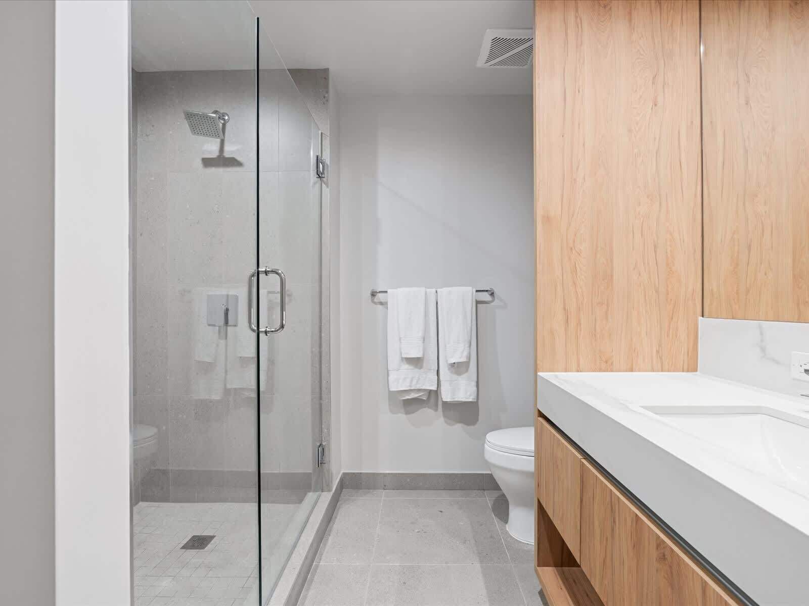 Une salle de bain moderne avec une douche à parois de verre, un lavabo blanc et des meubles en bois.