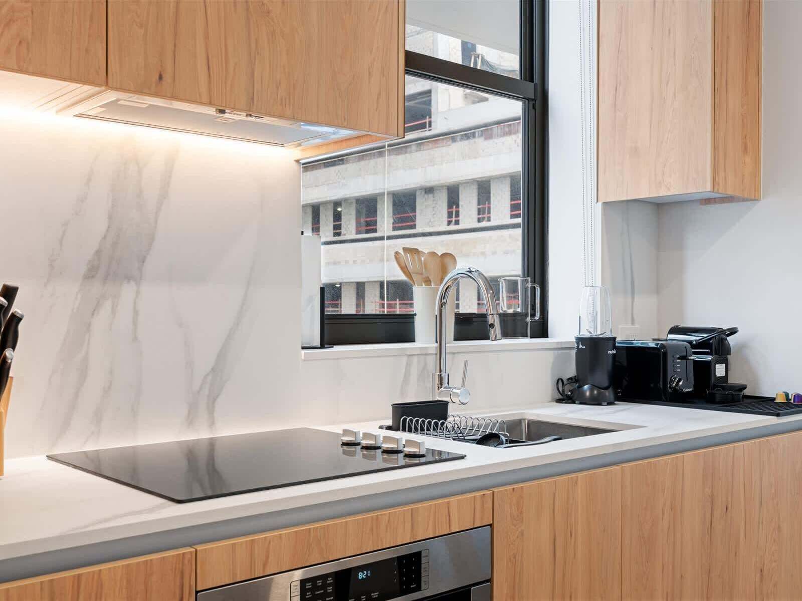 A modern kitchen with a built-in stove, a sink, and a window with a view of buildings.