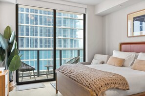 Ein Schlafzimmer mit großem Fenster, einem Bett, einem Sessel und einer Pflanze.