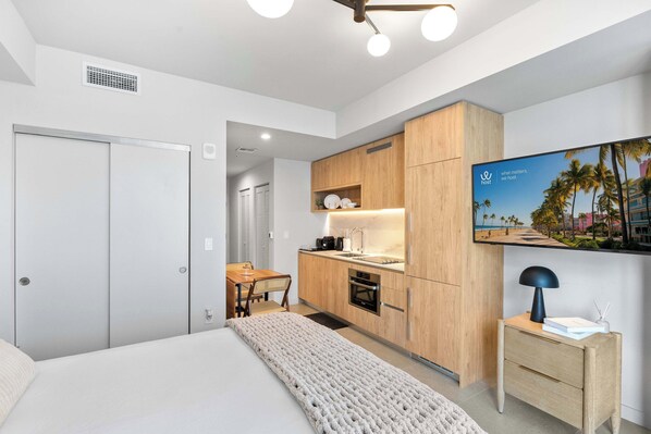 Ein modernes Hotelzimmer mit Bett, Küchenzeile, Essbereich und Fernseher.