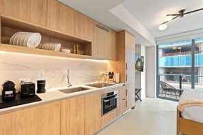 A modern kitchen with wooden cabinets, a built-in oven, a coffee machine, and a large window offering a view of the outside. - Modern Studio in Downtown Miami | Rooftop Pool (Miami)