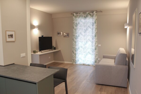 A modern living room with a flat-screen TV, a sofa, and a dining area with a table and chairs. - Borgo Predeschera (Lonato del Garda)