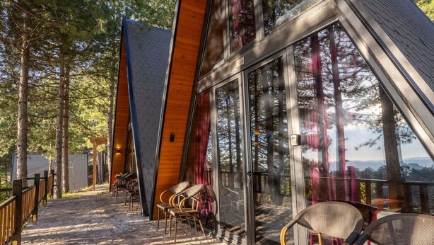 Un edificio moderno con grandes ventanales y fachada de madera, que cuenta con asientos al aire libre y vistas a árboles.