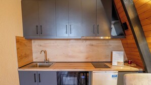 Una kitchenette compacta con gabinetes grises, un lavamanos de acero inoxidable, un microondas y un refrigerador pequeño.