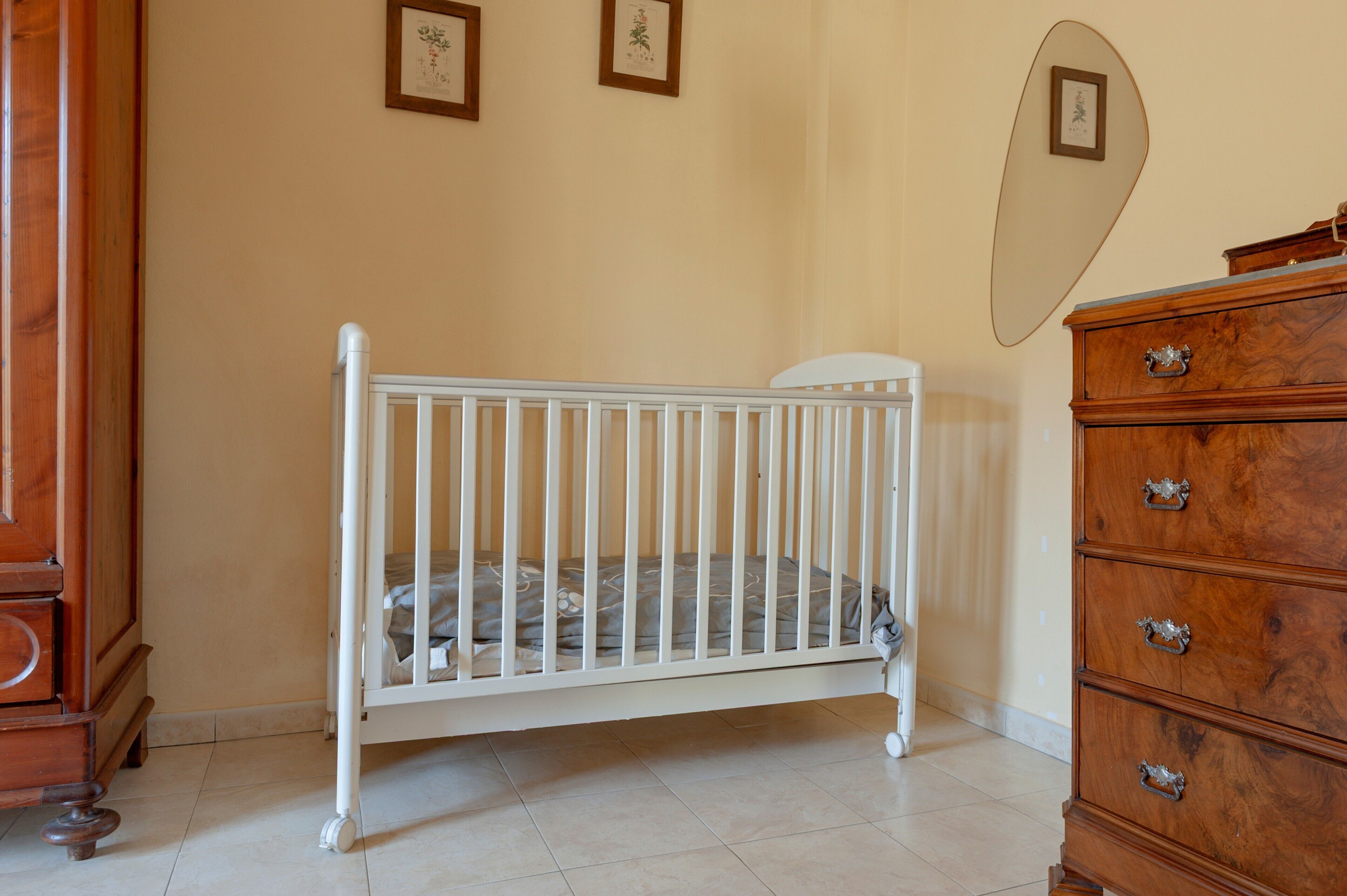 Ein Zimmer mit einem weißen Babybett, einem Holzkleiderschrank und gerahmten Bildern an der Wand.
