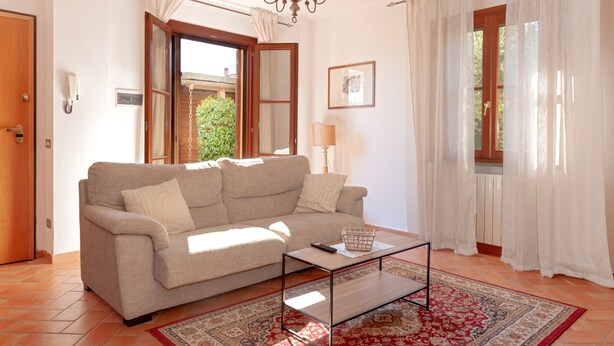 Un salon comprenant un canapé, une table basse, un lustre, une porte et une fenêtre avec des rideaux.