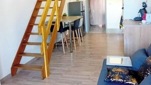 Un salon avec un canapé bleu, un escalier en bois et un coin repas comprenant des chaises et une table.