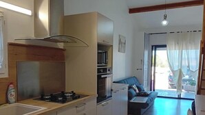 Une cuisine moderne équipée d’une cuisinière à gaz, d’un four et d’un micro-ondes, un coin repas avec un canapé bleu et une vue sur l’extérieur grâce à une porte vitrée.
