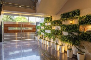 A modern lobby with a glass door entrance, potted plants, and a wall adorned with greenery and wall-mounted lights. - Ambassador Villa - An Experiential stay (Agra)