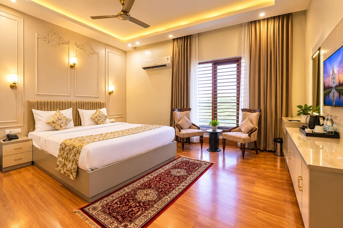 A hotel room with a large bed, two armchairs, a small table, a TV, and a window with curtains.