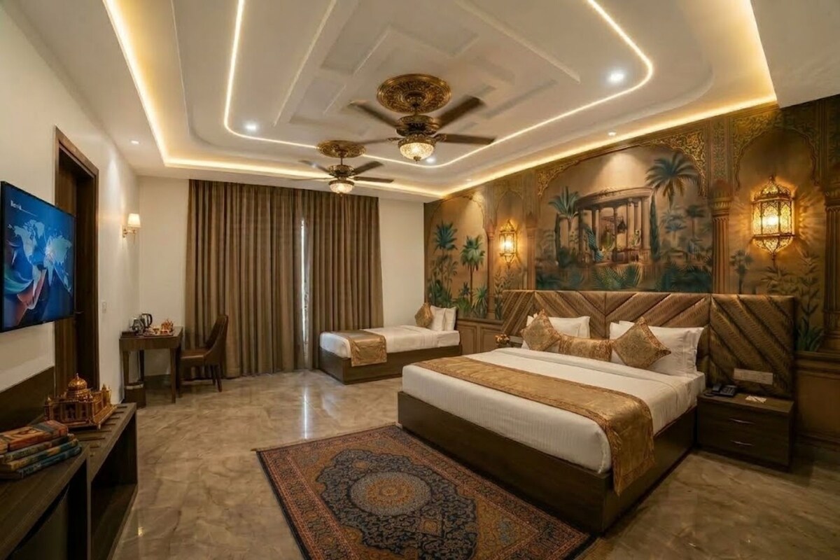A hotel room with a large bed, two smaller beds, a ceiling fan, a television, and a decorative wall mural.