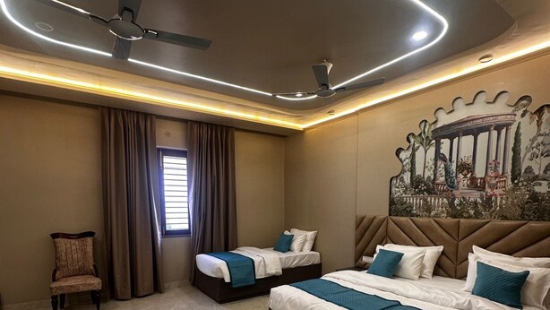 A hotel room with two beds, a ceiling fan, a large mural, and a window with curtains. - Ambassador Villa - An Experiential stay (Agra)