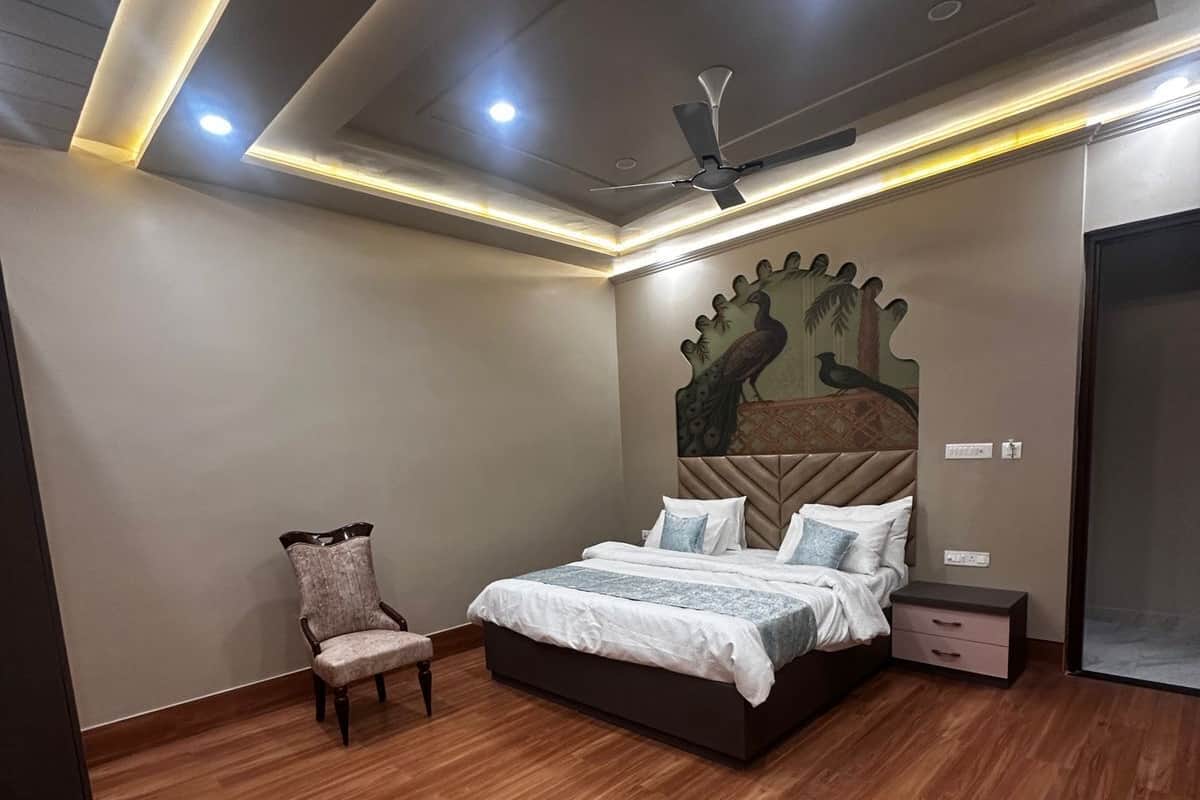 A bedroom with a bed, a chair, a nightstand, a ceiling fan, and a wall with a decorative mural.
