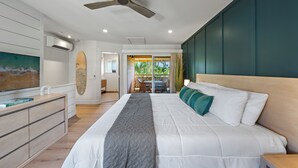 Quarto moderno com uma cama grande, ventilador de teto, TV e vista para uma varanda com móveis de exterior.