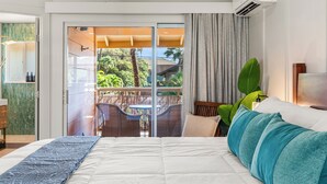 Ein Schlafzimmer mit einem großen Bett, einer Glastür, die zu einem Außenbereich mit Tisch und Stühlen führt, und Blick auf Grün.
