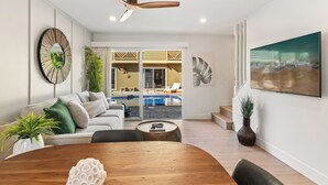 Ein modernes Wohnzimmer mit einem Holzesstisch, einer Couch und Blick auf einen Pool sowie eine Außenlounge.