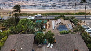 Une propriété située en bord de mer, dotée d’une piscine, de chaises longues et offrant une vue sur l’océan au coucher du soleil.