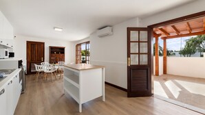 A modern kitchen with white cabinets, a wooden dining table, and chairs. There is a large window providing natural light and a view of the outdoors. - Villa Careva Suites 2 - VipVipVillas (Costa Teguise)