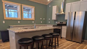 A kitchen with a granite countertop, stainless steel appliances, and wooden stools.