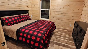 A wooden-paneled room with a bed, a dresser, and a ceiling fan.