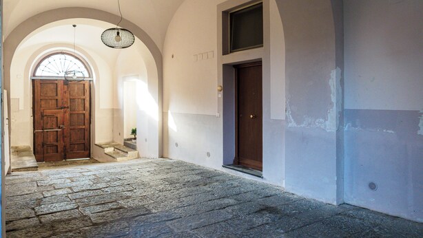 Un pasillo con suelo de piedra, una puerta de madera y una ventana con ventilador.