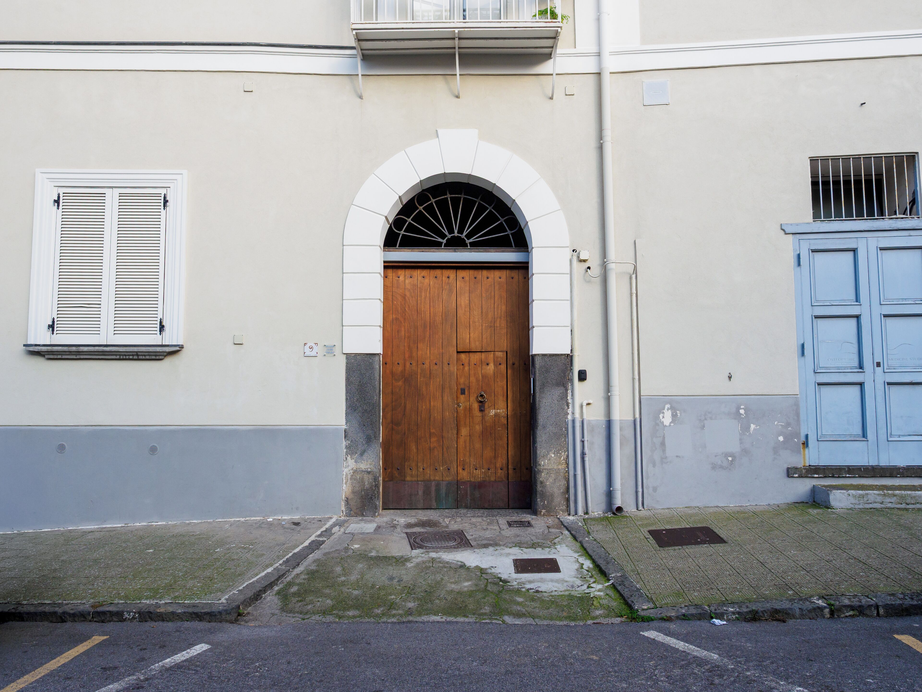 A building with a wooden door, a window with shutters, and a blue door.
