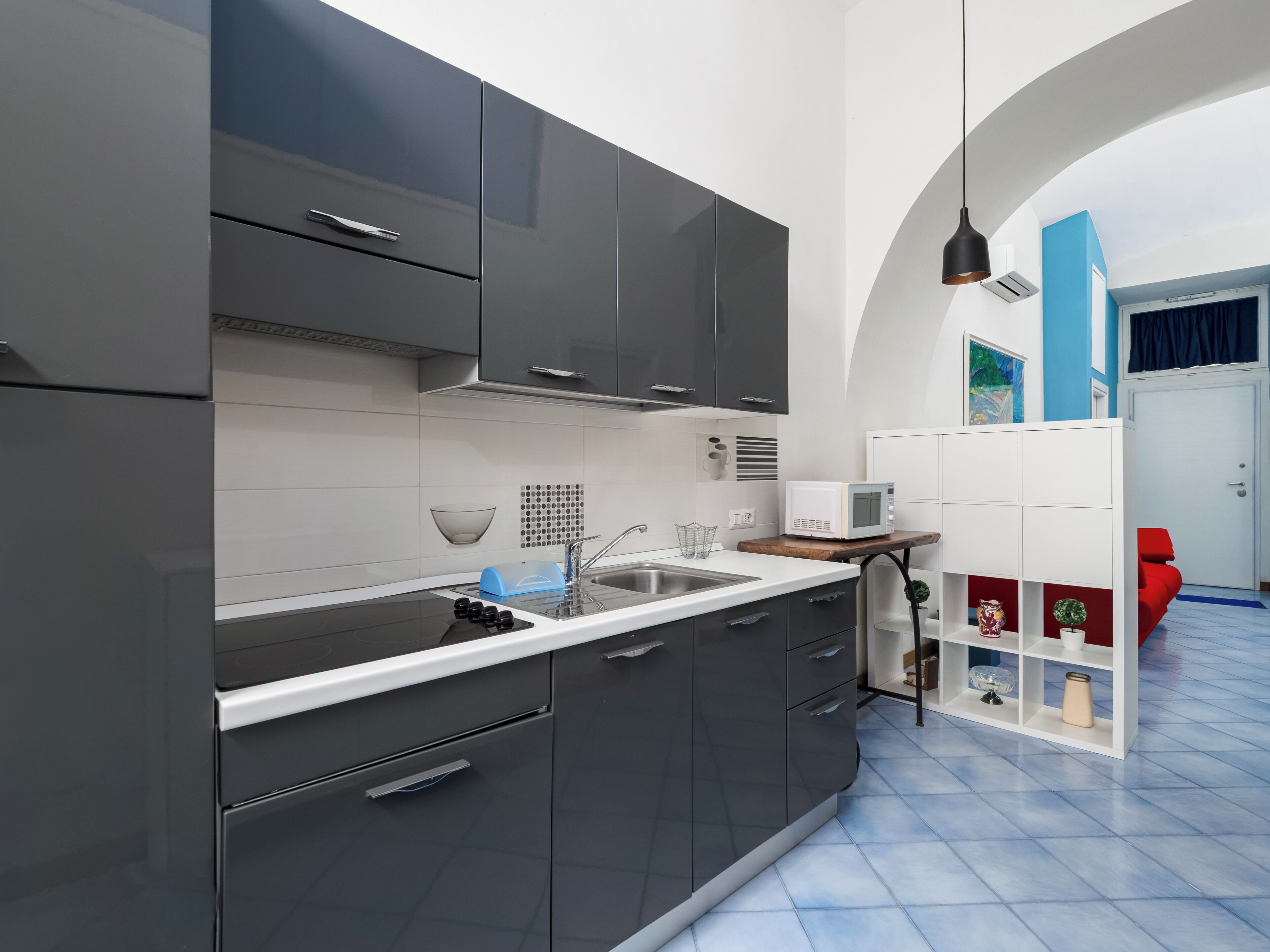 Una cocina moderna con armarios oscuros, una encimera blanca y un microondas en un estante de madera.