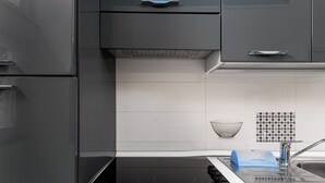 Una cocina moderna con tope de inducción negro, encimeras blancas y muebles grises.