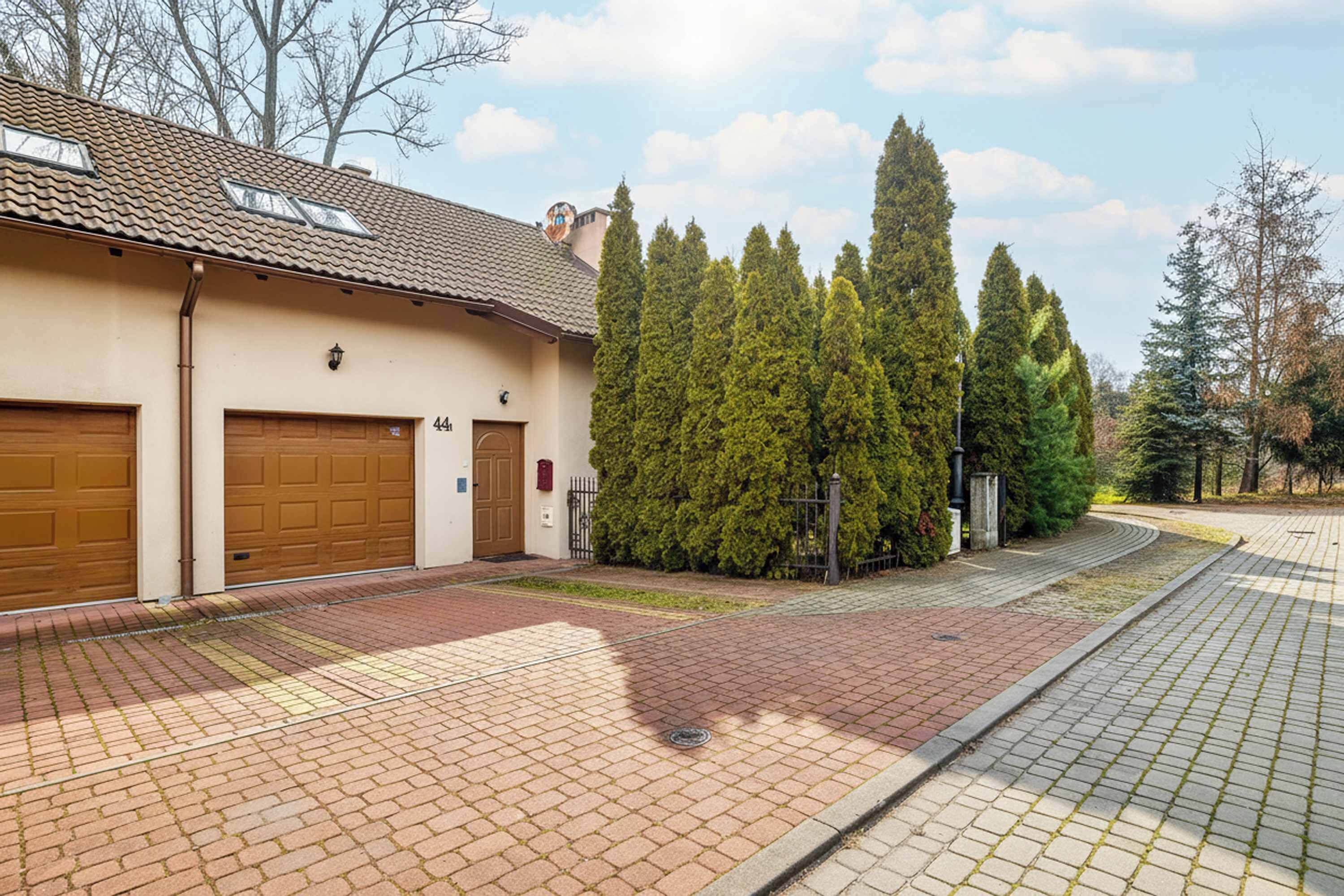 Um edifício residencial com duas garagens, telhado ladrilhado e gramado bem cuidado com árvores altas.