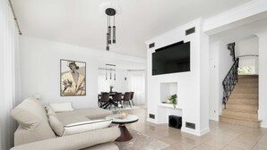 A modern living room with a beige sofa, a coffee table, a TV mounted on the wall, and a staircase leading to another level.