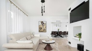 A modern living room with a beige sofa, a round coffee table, and a dining area in the background.