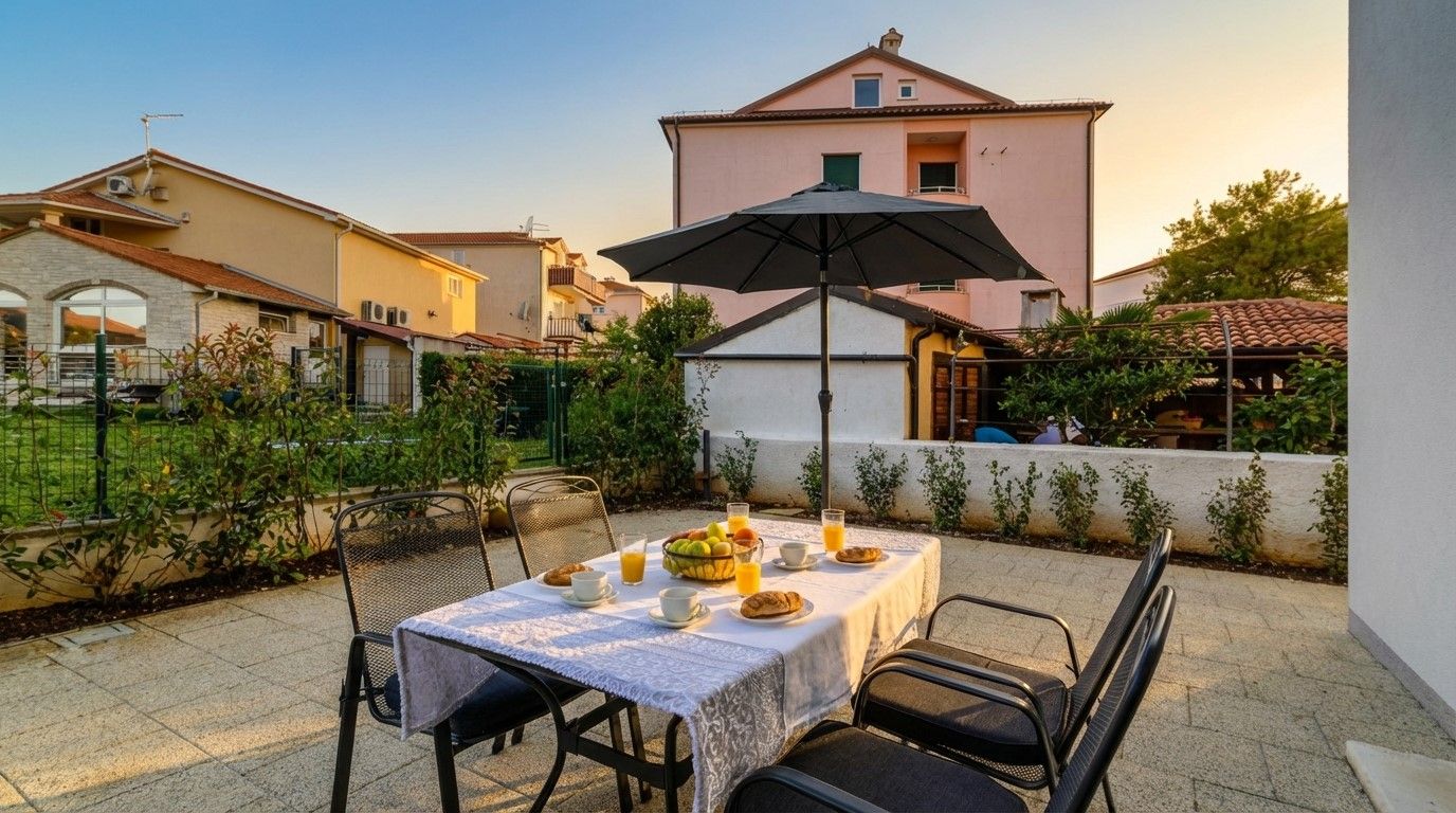 Une terrasse avec une table dressée pour le petit-déjeuner, entourée de chaises et agrémentée d’un parasol.