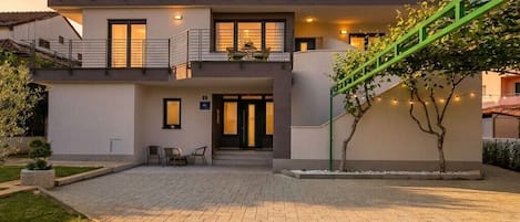 Een modern huis met twee verdiepingen, een balkon, een trap en een verharde oprit.